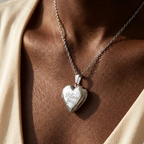 Heart-shaped silver locket with 'I love you' engraving on a person wearing a beige garment.
